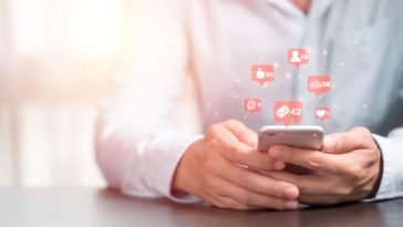 person holding a smartphone with social media icons coming out of it