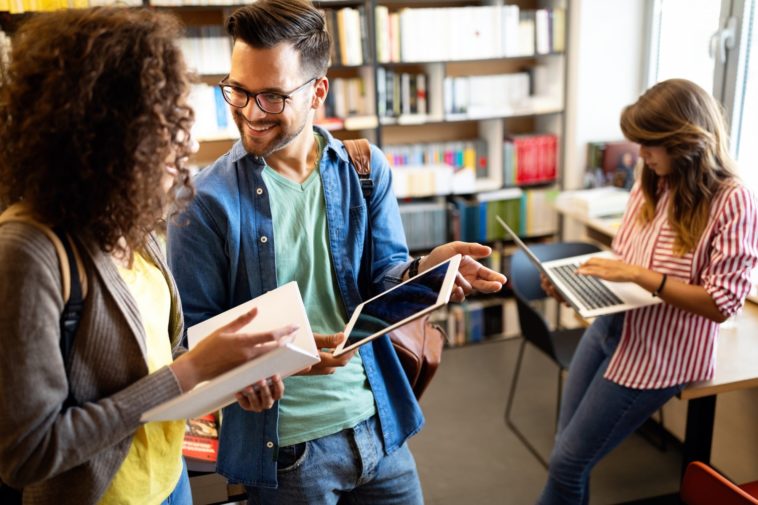 group of students in a library looking at a book, a laptop and a tablet