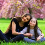 young woman and a little girl sitting on the grass in a park