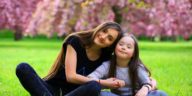 young woman and a little girl sitting on the grass in a park