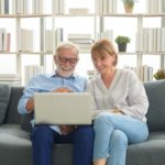 senior couple sitting on a couch using a laptop