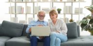 senior couple sitting on a couch using a laptop