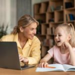 woman and little girl sitting at a desk and using a laptop to learn