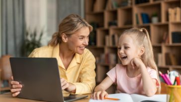 woman and little girl sitting at a desk and using a laptop to learn