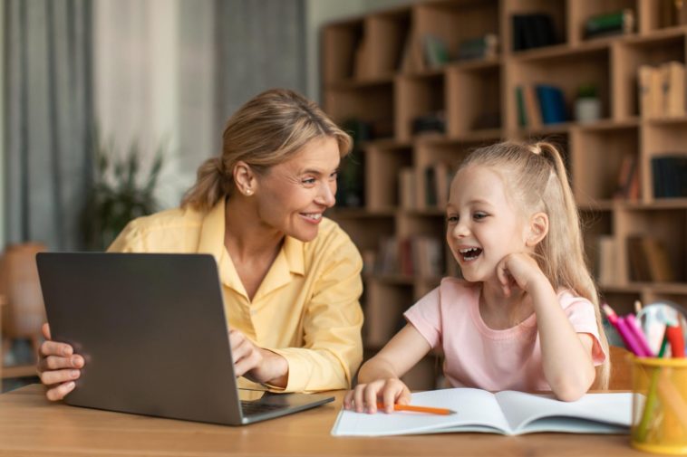 woman and little girl sitting at a desk and using a laptop to learn