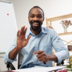 man sitting at a desk in front of a computer smiling and waving