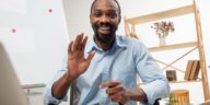 man sitting at a desk in front of a computer smiling and waving