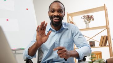 man sitting at a desk in front of a computer smiling and waving