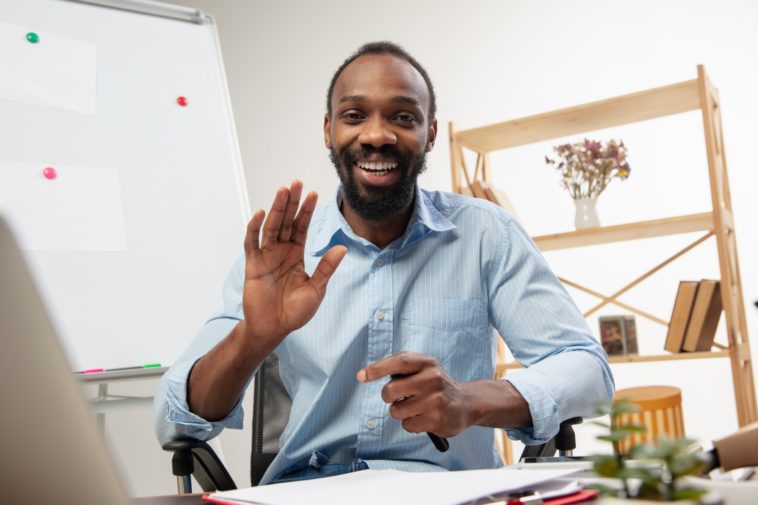 man sitting at a desk in front of a computer smiling and waving