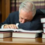 man sleeping on a desk surrounded by books