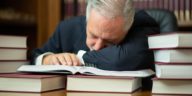 man sleeping on a desk surrounded by books