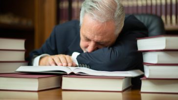 man sleeping on a desk surrounded by books