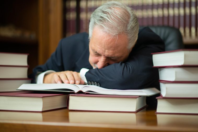 man sleeping on a desk surrounded by books