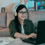 woman with headphones typing on a laptop