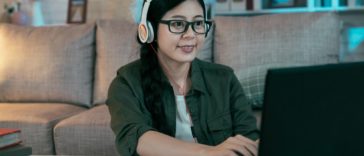 woman with headphones typing on a laptop