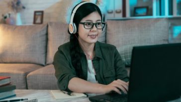 woman with headphones typing on a laptop