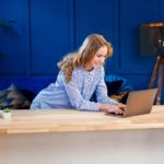 woman using a laptop at a desk with clothes in the background