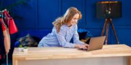 woman using a laptop at a desk with clothes in the background