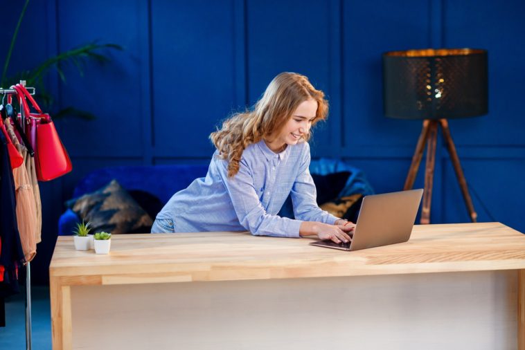 woman using a laptop at a desk with clothes in the background