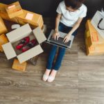 woman with a laptop in her lap surrounded by boxes