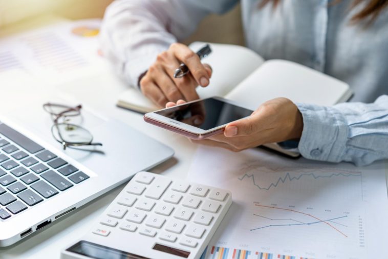 woman working at a desk with a phone, laptop and calculator