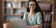 smiling woman with headphones sitting behind a desk with a laptop