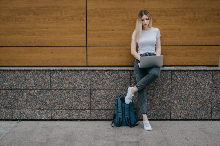 woman leaning on a wall with a laptop in her hands