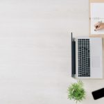 bird view of laptop, phone, plant, coffee and someone writing in a notebook