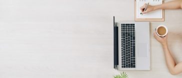 bird view of laptop, phone, plant, coffee and someone writing in a notebook