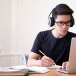 young man with headphones looking at a laptop and writing