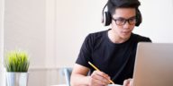 young man with headphones looking at a laptop and writing