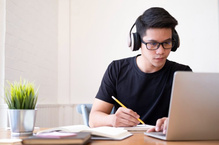 young man with headphones looking at a laptop and writing