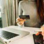 woman sitting at a desk holding a credit card and using a tablet