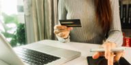 woman sitting at a desk holding a credit card and using a tablet