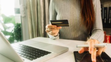 woman sitting at a desk holding a credit card and using a tablet