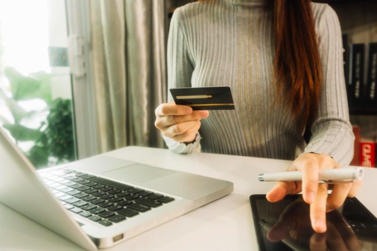 woman sitting at a desk holding a credit card and using a tablet