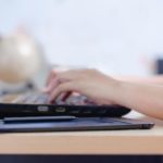 person typing on a laptop with a coffee cup next to it