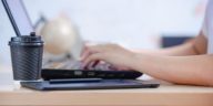 person typing on a laptop with a coffee cup next to it