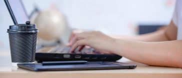 person typing on a laptop with a coffee cup next to it