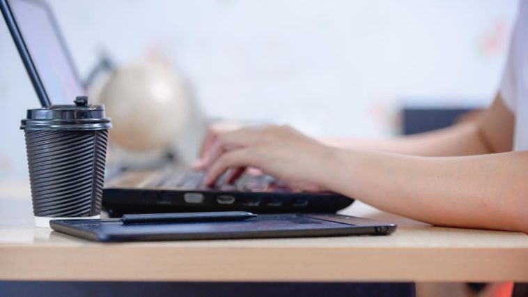 person typing on a laptop with a coffee cup next to it