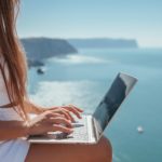 digital nomad woman sits on rocks by the sea