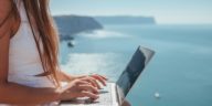 digital nomad woman sits on rocks by the sea