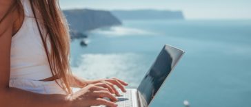 digital nomad woman sits on rocks by the sea
