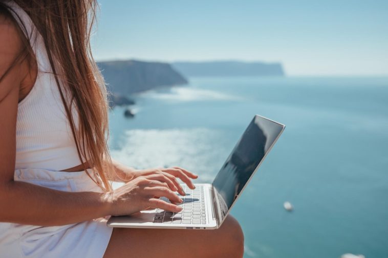 digital nomad woman sits on rocks by the sea