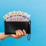 hand holding a black wallet with british pounds