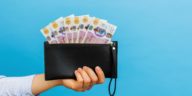 hand holding a black wallet with british pounds