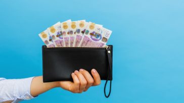 hand holding a black wallet with british pounds