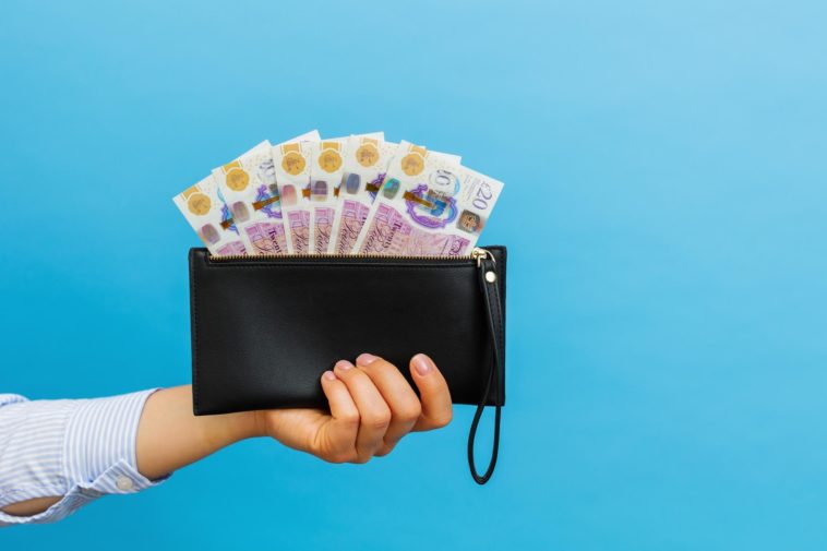 hand holding a black wallet with british pounds