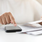 woman holding a paper bill invoice and using a smartphone