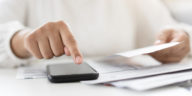 woman holding a paper bill invoice and using a smartphone